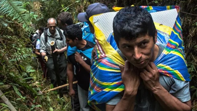 Fila de porteadores avanzando con carga en el bosque denso del Toporaké